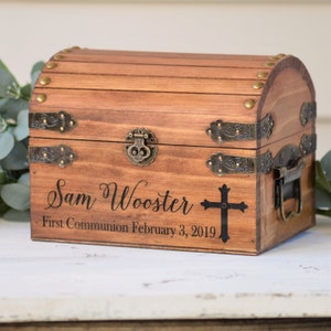Puede incluir: Un cofre del tesoro de madera con tapa con bisagras, detalles en lat&oacute;n y un dise&ntilde;o de cruz. El cofre est&aacute; personalizado con el nombre "Sam Wooster" y el texto "Primera Comuni&oacute;n 3 de febrero de 2019".