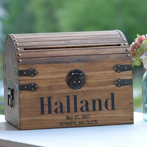 Peut inclure: Un coffre au tr&eacute;sor en bois avec des accents m&eacute;talliques et une fente pour les cartes. Le coffre est personnalis&eacute; avec le nom "Halland" et la date "May 27, 2017".