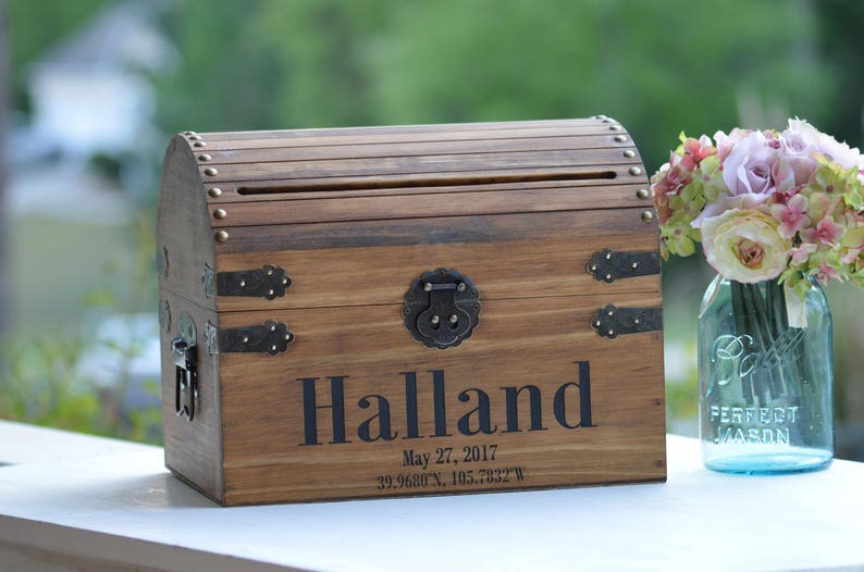 Peut inclure: Un coffre au tr&eacute;sor en bois avec des accents m&eacute;talliques et une fente pour les cartes. Le coffre est personnalis&eacute; avec le nom "Halland" et la date "May 27, 2017".