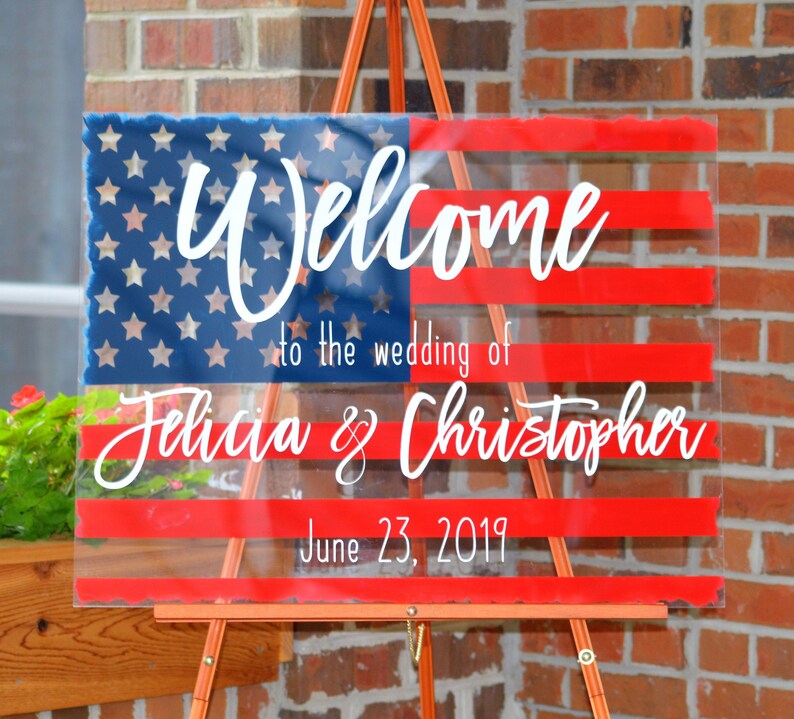 May include: A clear acrylic wedding welcome sign featuring a red, white and blue American flag design. The sign reads "Welcome to the wedding of Felicia & Christopher June 23, 2019".