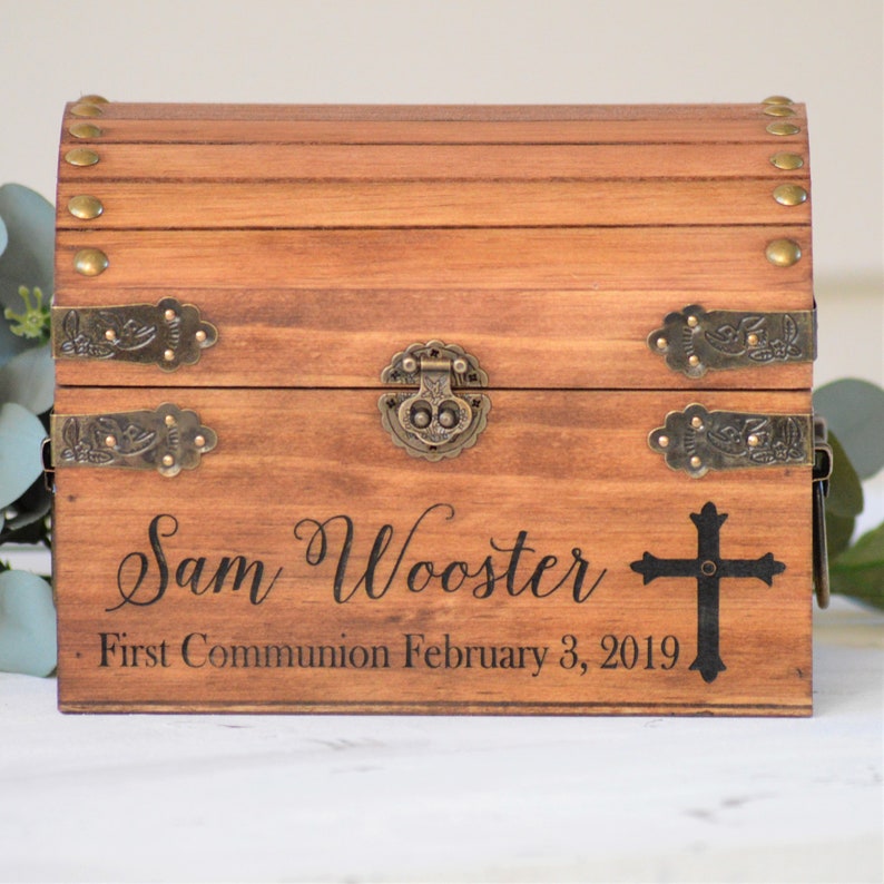 Puede incluir: Un cofre del tesoro de madera con tapa con bisagras, detalles en lat&oacute;n y un dise&ntilde;o de cruz. El cofre est&aacute; grabado con el nombre "Sam Wooster" y el texto "Primera Comuni&oacute;n 3 de febrero de 2019".