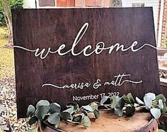 May include: A rustic brown wooden welcome sign with white calligraphy. The sign reads "welcome" in a cursive font and "marisa & matt" with the date "November 17, 2022" below.
