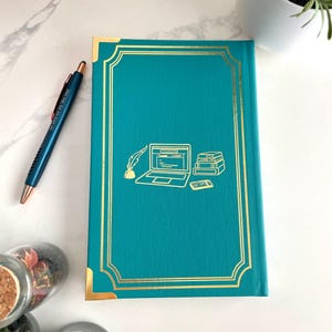 Peut inclure: Journal &agrave; couverture rigide bleu turquoise avec des accents dor&eacute;s et une illustration dor&eacute;e d'un ordinateur portable, de livres et d'un stylo sur la couverture.