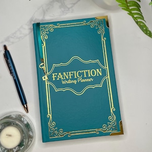 Pode incluir: Um di&aacute;rio de capa dura azul turquesa com detalhes dourados e o texto "FANFICTION Writing Planner" na capa.