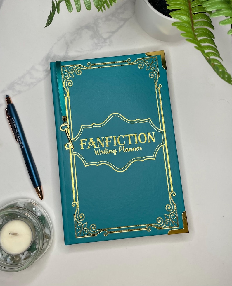 Pode incluir: Um di&aacute;rio de capa dura azul turquesa com detalhes dourados e o texto "FANFICTION Writing Planner" na capa.