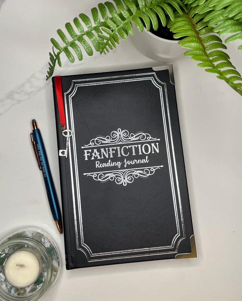 Peut inclure: Un journal noir avec des accents argent&eacute;s et le texte "FANFICTION Reading Journal" sur la couverture. Un ruban rouge est attach&eacute; au journal avec un charme de cl&eacute; argent&eacute;e.