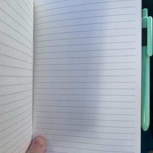 May include: Open notebook with lined pages, a pen is clipped to the side. The notebook has a white cover with the words "date:" and "page:" printed at the top. The pen is a light green color.