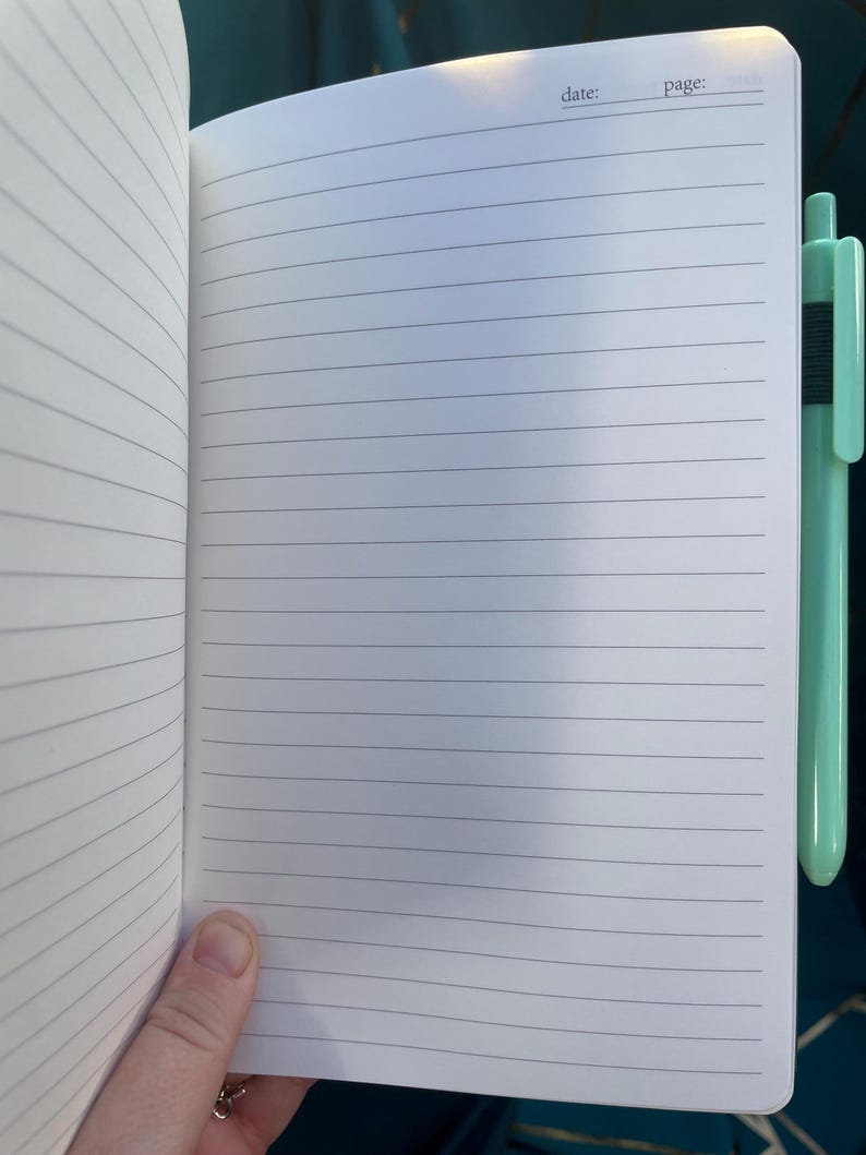 May include: Open notebook with lined pages, a pen is clipped to the side. The notebook has a white cover with the words "date:" and "page:" printed at the top. The pen is a light green color.