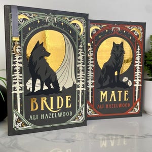 Może przedstawiać: Dwie książki w twardej oprawie z czarnymi okładkami. Jedna książka ma napis "BRIDE" złotymi literami, druga "MATE". Obie książki przedstawiają czarną sylwetkę wilka na tle złotego księżyca, z nazwiskiem autora poniżej.