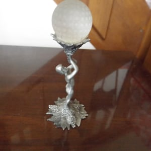 May include: A silver figurine of a woman holding a clear glass orb on a leaf-shaped base.