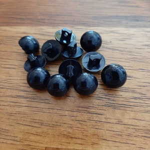 May include: A group of black plastic buttons with a star design on the top. The buttons have a shank on the back for sewing.
