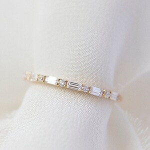 May include: A delicate gold band ring with a row of small, rectangular-shaped diamonds.