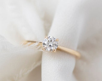 May include: A simple gold band ring with a single round diamond in the center.
