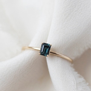 Puede incluir: Un anillo de oro con una piedra rectangular de color azul oscuro.