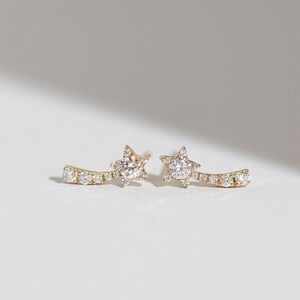 May include: A pair of gold earrings with a curved line of small diamonds and a star-shaped diamond at the end of each earring.