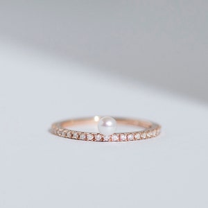 May include: A delicate gold ring with a single pearl and a band of small diamonds.
