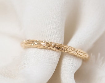 May include: A thin gold band ring with a textured, tree bark-like design.