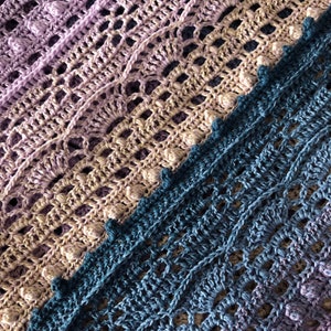 May include: A crocheted blanket with a gradient of purple, brown, and blue colors. The blanket is made with a delicate stitch pattern and has a textured surface.