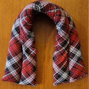May include: Red and black tartan neck wrap with a white and grey tartan design. The wrap is shaped like a horseshoe and is filled with rice or beans for warmth.
