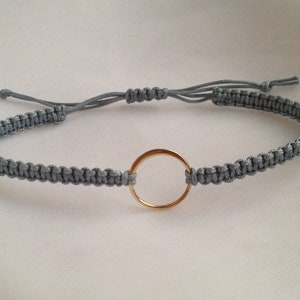May include: A gray braided bracelet with a gold circle charm.