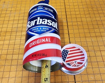 Peut inclure: Une boîte de crème à raser Barbasol rouge, blanche et bleue avec les mots "Thick & Rich Shaving Cream" et "Original" imprimés sur la boîte. La boîte est ouverte et un mètre ruban est à côté. La boîte est sur une surface à carreaux brun et blanc.
