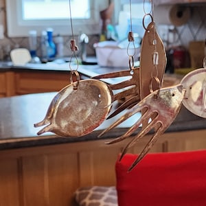 May include: A metal wind chime with multiple fish-shaped ornaments hanging from a string. The ornaments are made from recycled silverware and have a shiny, metallic finish.