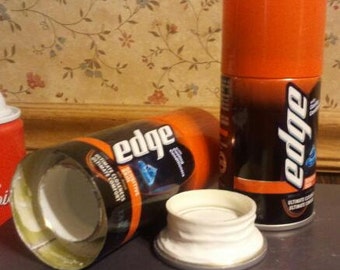 May include: Two orange and black shaving cream cans with the word "Edge" printed on them. One can is open and the top is removed. The can is empty. The other can is closed.