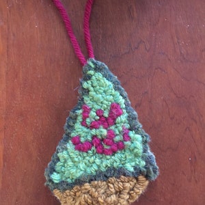 Op de afbeelding: Een groene en bruine kerstboomversiering van garen met een rood garenontwerp. De versiering heeft een rode garenlus om op te hangen.