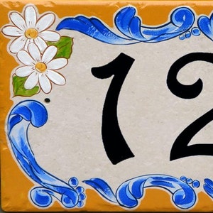 May include: A white ceramic house number sign with blue and yellow floral accents. The number 123 is painted in black.