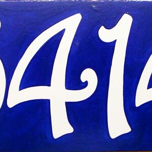 May include: White ceramic tile with the number 5414 painted in a white cursive font on a royal blue background.