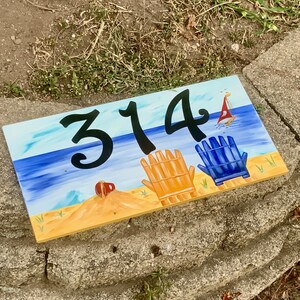 Beach decors address plaque with aqua sky, blue water and two chairs, a boat and a pail.
