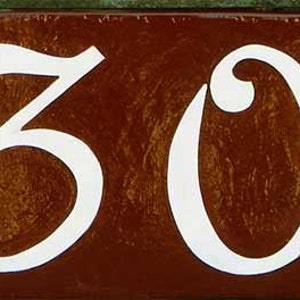 May include: A brown ceramic house number plaque with white painted numbers "30" in a decorative script font.