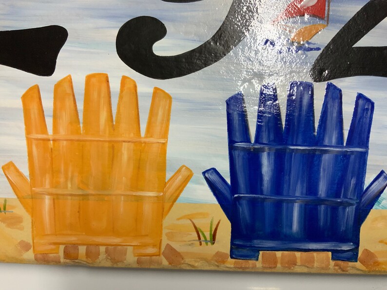 May include: Two painted wooden chairs, one yellow and one blue, are on a beach scene. The chairs are facing away from the viewer.