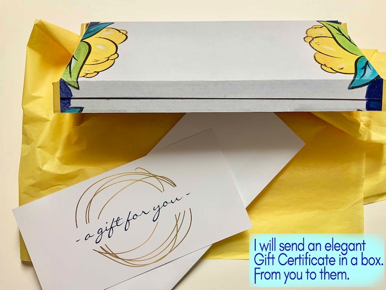 May include: A rectangular gift box with a white lid featuring yellow lemon and green leaf illustrations at the corners. Below the box lies a white card with the text "a gift for you" in black script, surrounded by a gold circular line design.