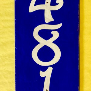 May include: A blue ceramic tile with the number 481 painted in white. The tile is a house number.