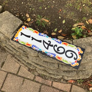 May include: Rectangular address sign with the number 1466 in black against a white background. The sign has a black border and is decorated with colorful floral patterns. The sign is placed on a stone wall.
