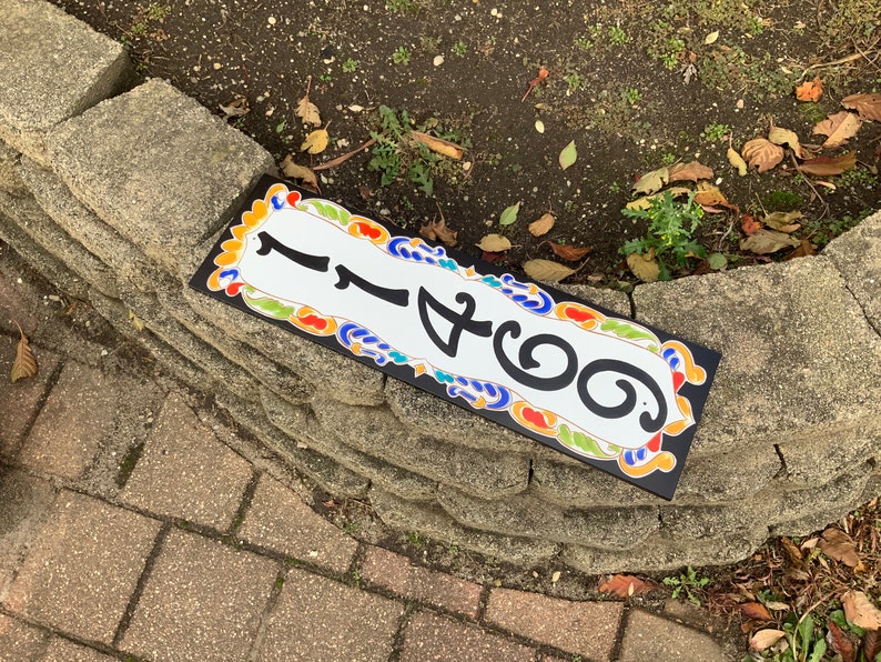 May include: Rectangular address sign with the number 1466 in black against a white background. The sign has a black border and is decorated with colorful floral patterns. The sign is placed on a stone wall.