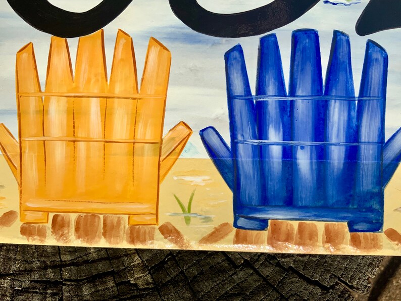 May include: A painted wooden sign with two beach chairs, one yellow and one blue, on a sandy beach background.