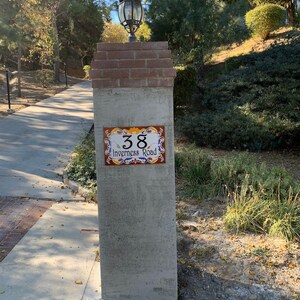May include: A gray concrete pillar with a brick top and a decorative tile sign that reads "38 Inverness Road". A lamp post with a glass lantern is mounted on the pillar.