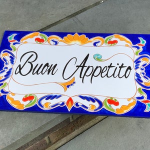 May include: A blue and white ceramic tile with a decorative border and the words "Buon Appetito" in black script.
