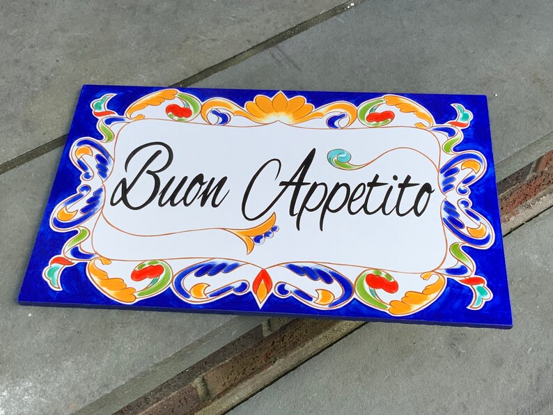 May include: A blue and white ceramic tile with a decorative border and the words "Buon Appetito" in black script.