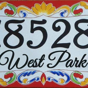 May include: A white ceramic house number sign with black painted numbers "18528" and the text "West Park" in a decorative script font. The sign is surrounded by a colorful, ornate border with red, yellow, blue, and green accents.