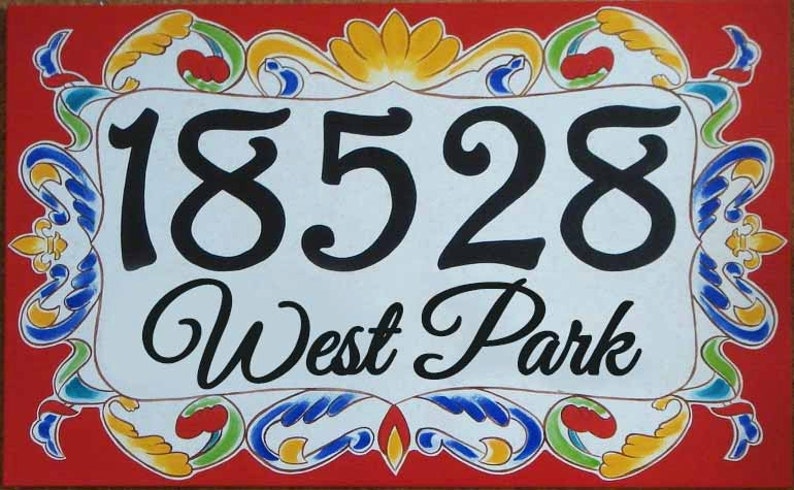 May include: A white ceramic house number sign with black painted numbers "18528" and the text "West Park" in a decorative script font. The sign is surrounded by a colorful, ornate border with red, yellow, blue, and green accents.