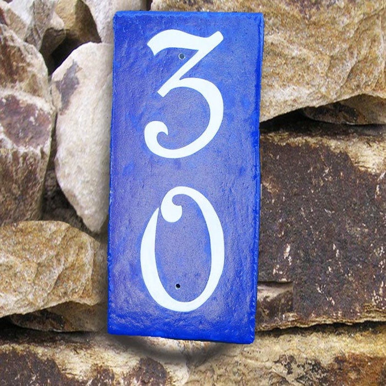 May include: A blue ceramic house number sign with white painted numbers, the number is 30.