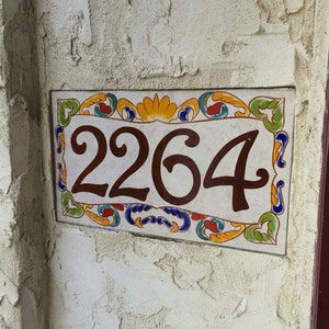 May include: A rectangular ceramic house number plaque featuring the digits 2264 in dark brown. The plaque has a white background with a decorative border painted in vibrant yellow, blue, red, and green floral and scroll patterns.