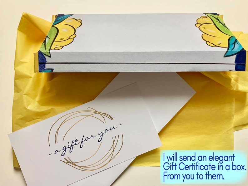 May include: A white gift certificate with gold lettering that says "a gift for you" inside a white box with a lemon design. The box is wrapped in yellow tissue paper.