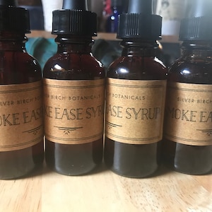 Könnte beinhalten: Vier braune Glasflaschen mit Tropfern und braunen Papierretiketten. Die Etiketten lauten "Smoke Ease Syrup" und "Silver Birch Botanicals".
