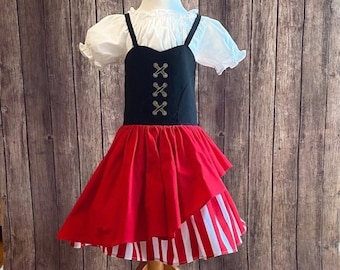 Pode incluir: Uma saia de listras vermelhas e brancas com um corpete preto e detalhes dourados. O corpete tem um design cruzado e a saia tem uma bainha com babados.