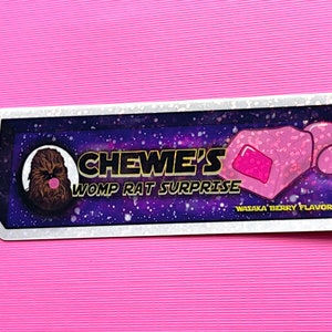 May include: A white sticker with a galaxy background featuring a cartoon image of Chewbacca with a pink bubble and a pink Womp Rat Surprise candy. The text on the sticker reads "Chewie's Womp Rat Surprise" and "Wataka Berry Flavored".