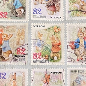 Può includere: Nove francobolli giapponesi vintage con illustrazioni di conigli. Ogni francobollo mostra il numero "82" e testo giapponese. I francobolli sono disposti in una griglia 3x3 su uno sfondo grigio chiaro.